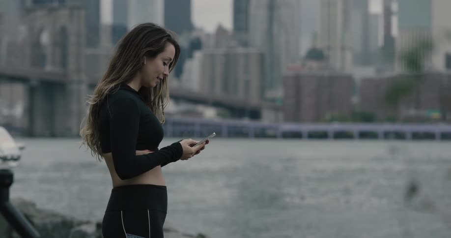 Woman stops jogging and checks phone at city riverbank