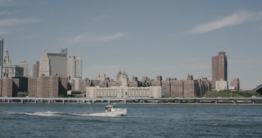 A boat drives under the brooklyn bridge with the city skyline behind