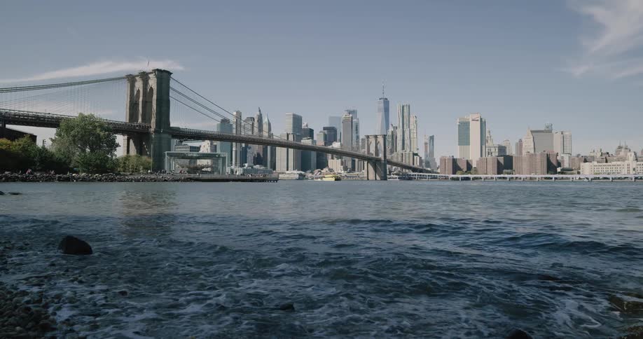 Small waves wash upon the rocky shoreline as a major metropolitan with many tall buildings towers across the water