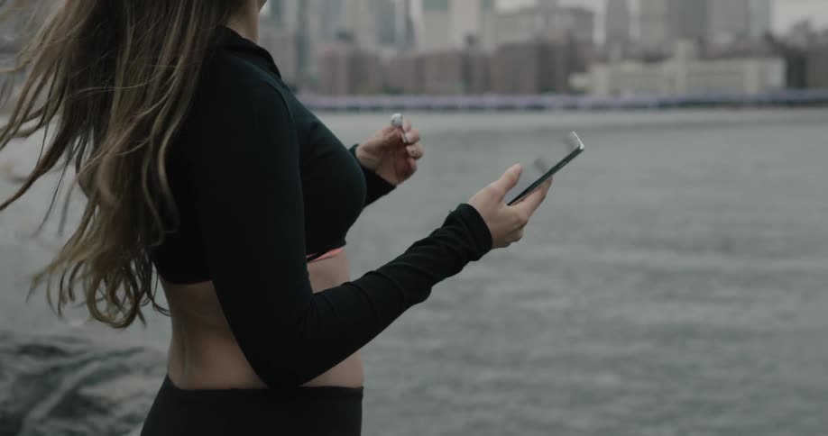 A woman puts an earbud in and looks at her phone