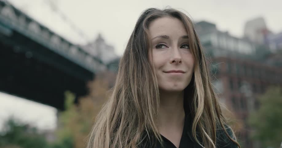 Woman looks around and smile under the bridge in the city on acloudy day