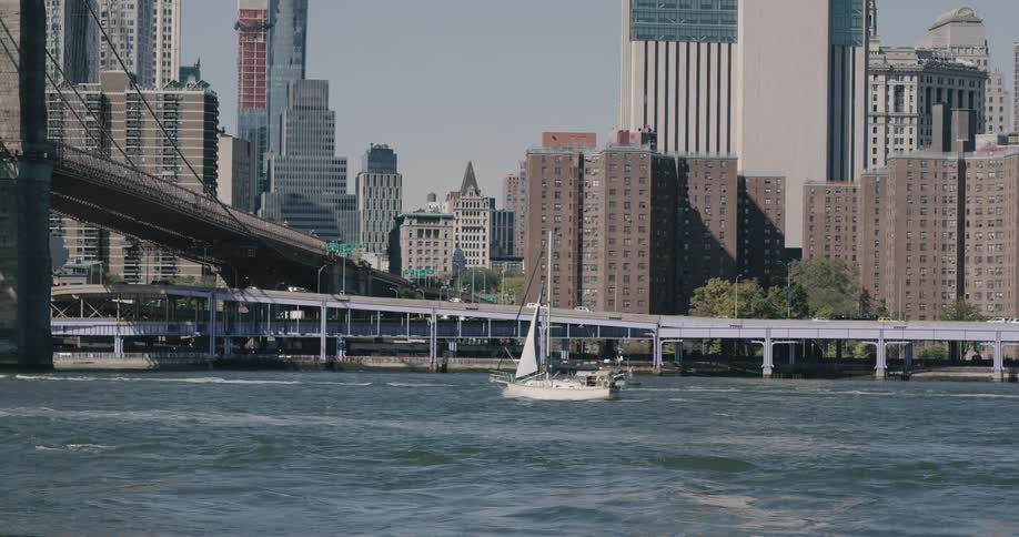 A sailboat sails on calm water near an urban landscape
