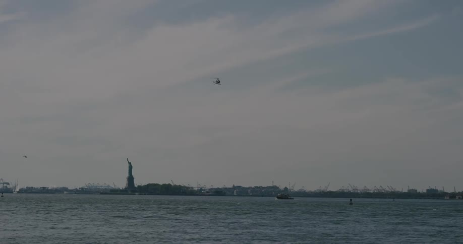A helicopter flies over water near the statue of liberty