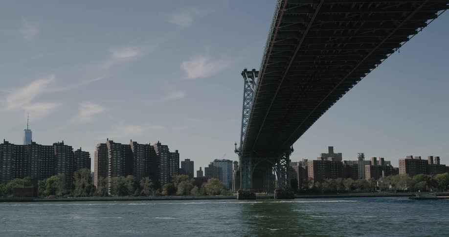 A river flows beneath a large city bridge in the daytime