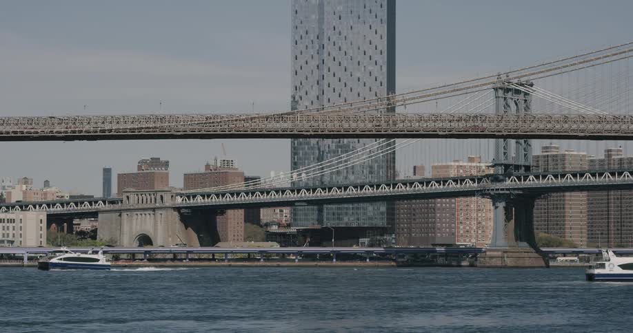 A blue and white boat traverses some water near a suspension bridge