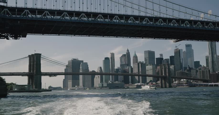 Boats cross under parallel suspension bridge with downtown in background