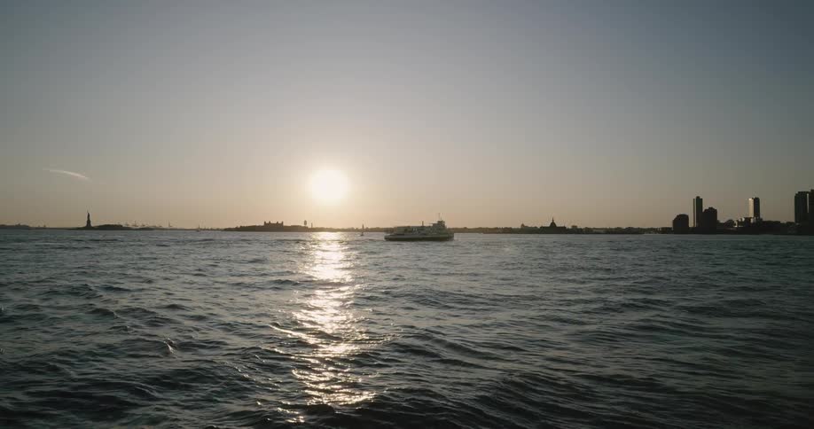 Skyline of the city with tall buildings and the ferry floats along the sea at sunset
