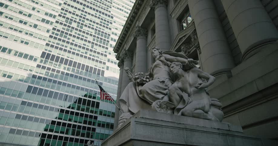 A statue with a flag mounted on it sits in front of a highrise building