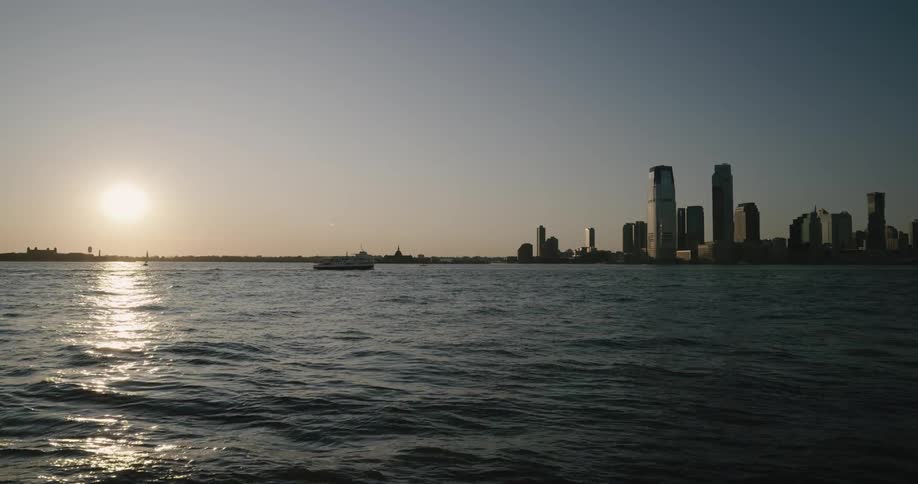 Skyline of the city with tall buildings and skyscrapers while ferries float along the sea at sunset