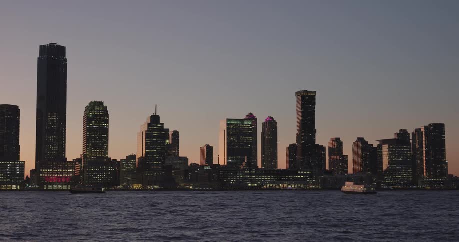 Boats cross ocean in front of city at dusk