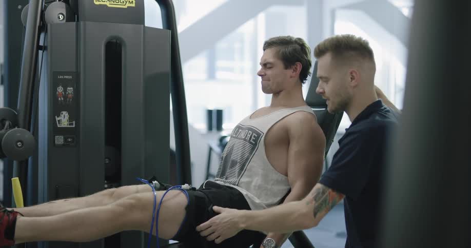 A man goes through an intense leg workout while a trainer assists