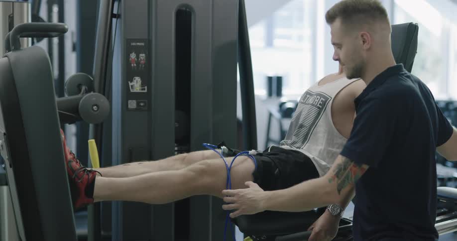 A man sits on a leg press machine with his trainer next to him while working out