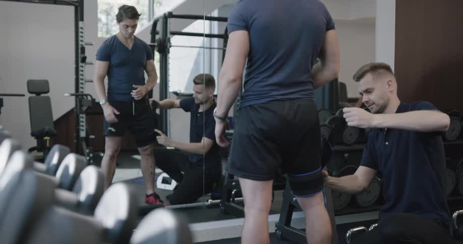 A young man puts a brace on another mans leg before exercising