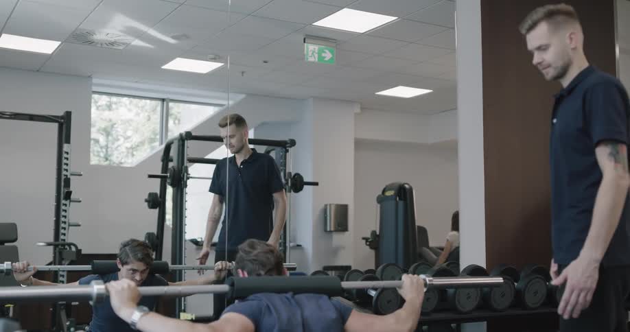 Man works out with a barbell while another man coaches him