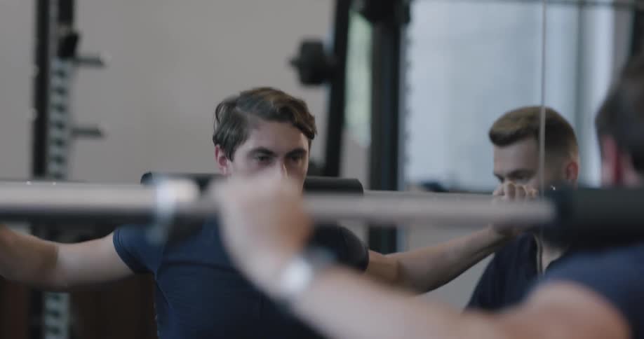 A man does a squat with his trainer next to him on a weight machine
