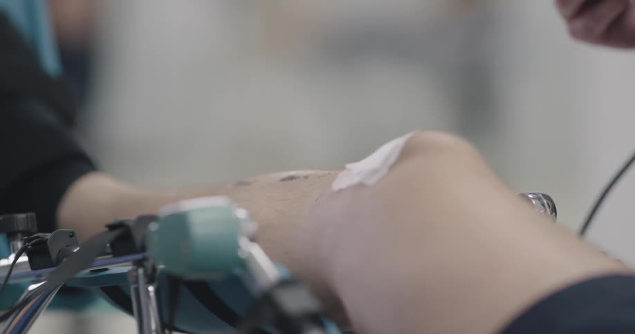A man looks at a device while another man lies with his knee in a brace