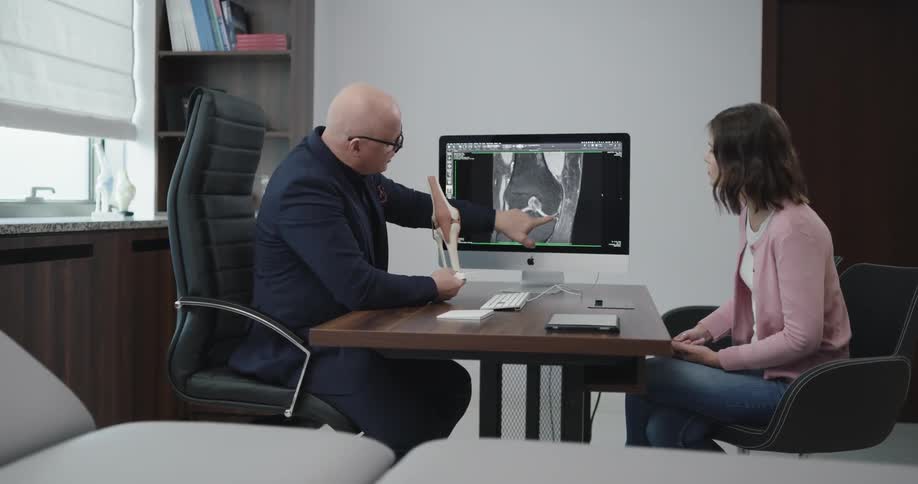 A doctor is showing a model of a knee to a patient in his office
