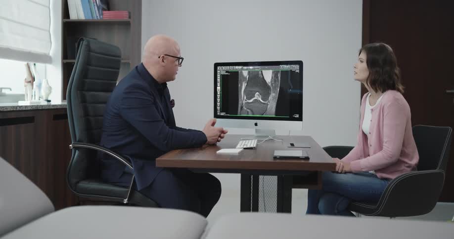 A man explains an image of a joint to a woman in his office
