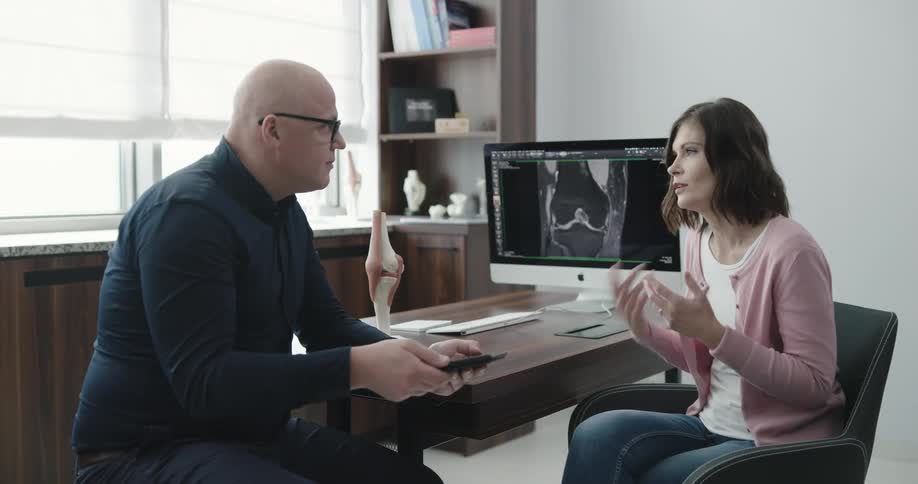 A woman speaks with a physician about her knee while sitting in a doctors office