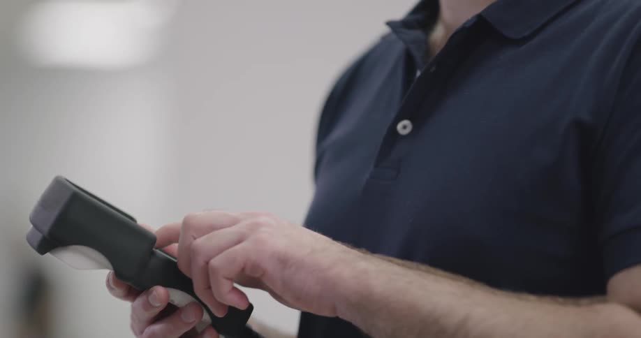 A bearded man holds a device in his had as he presses buttons and then nods reassuringly as he speaks to another person