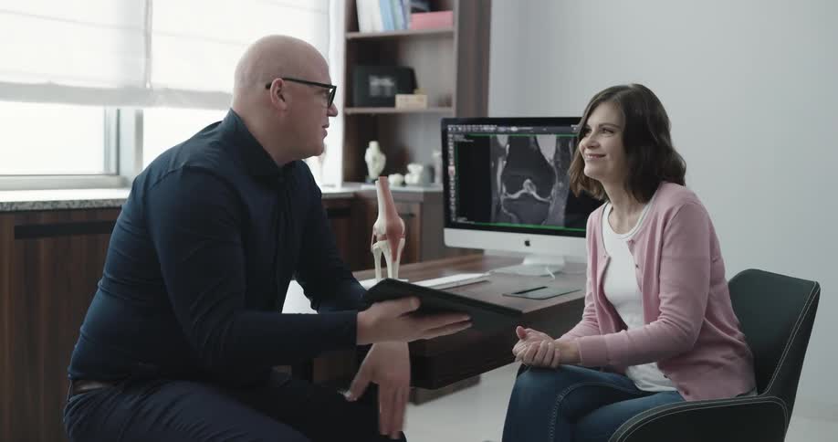 Bald doctor explaining something with his tablet to the patient at the clinic