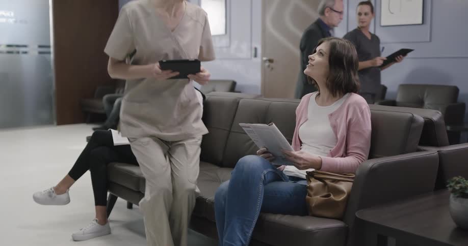 Nurse approaches patient in clinic waiting room to help her fill out form