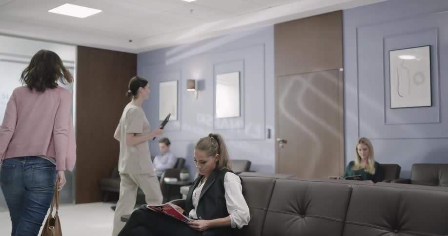 A woman sits in a waiting room and hands a tablet to a nurse
