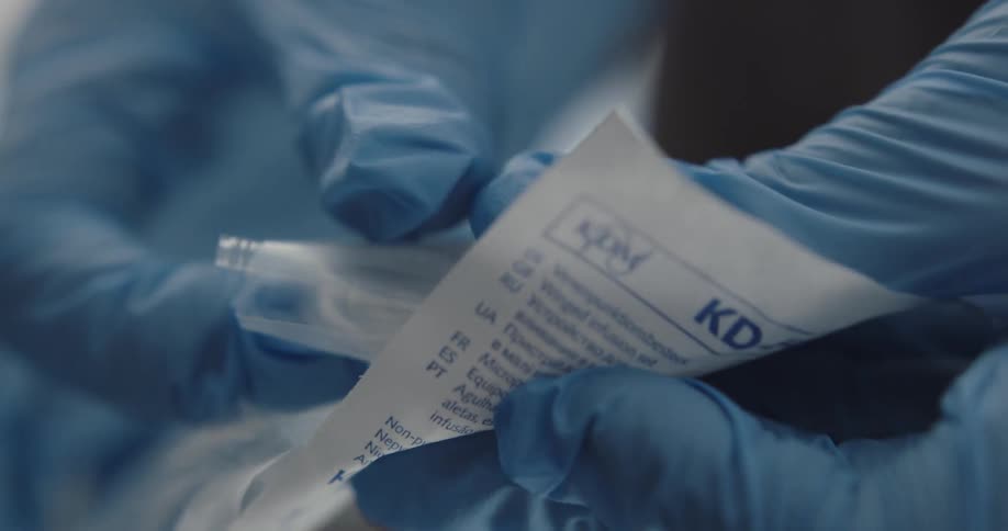 A nurse opens a plastic package with an iv needle and tube