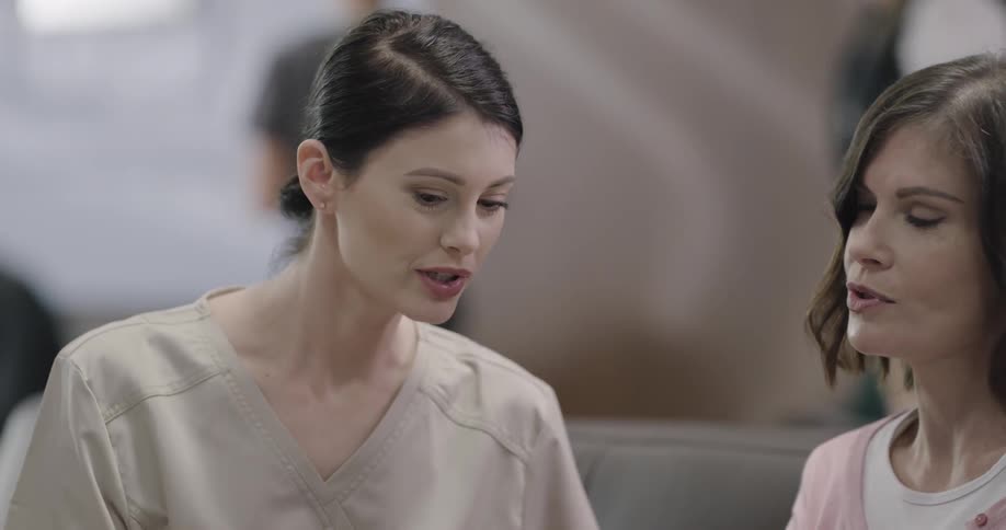 A woman wearing hospital scrubs discusses something with another woman on a tablet
