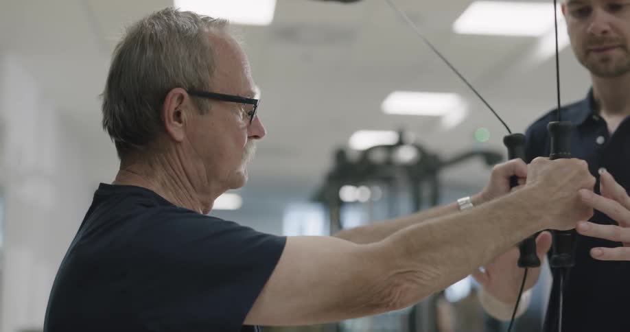 Old man with glasses work out at the gym with an assistance