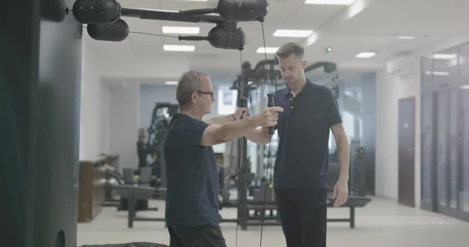 A physical therapist works with a man on fitness equipment in a clinic