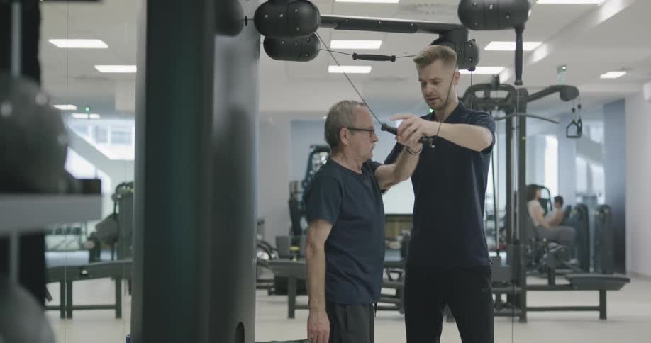 A trainer teachers a man how to use exercise equipment correctly