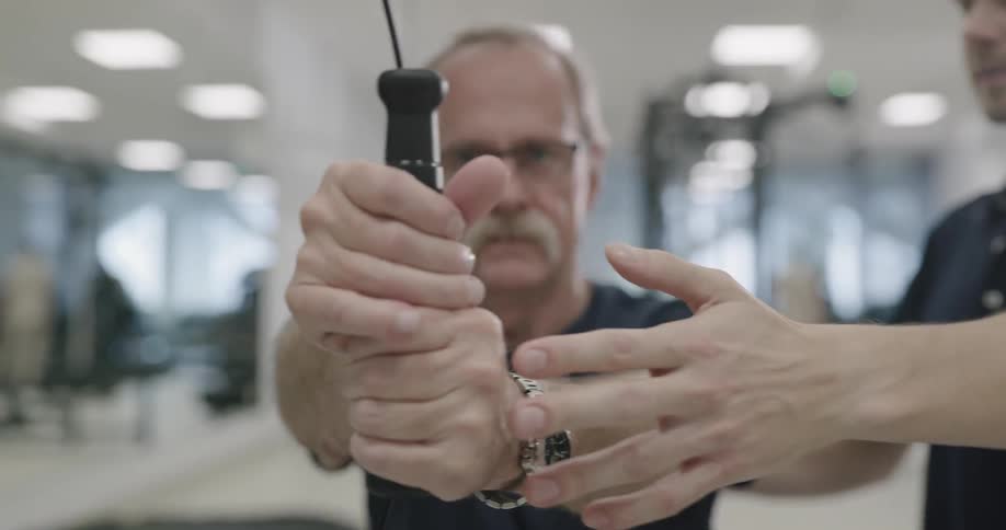 A male uses a machine in the gym with a physical therapist