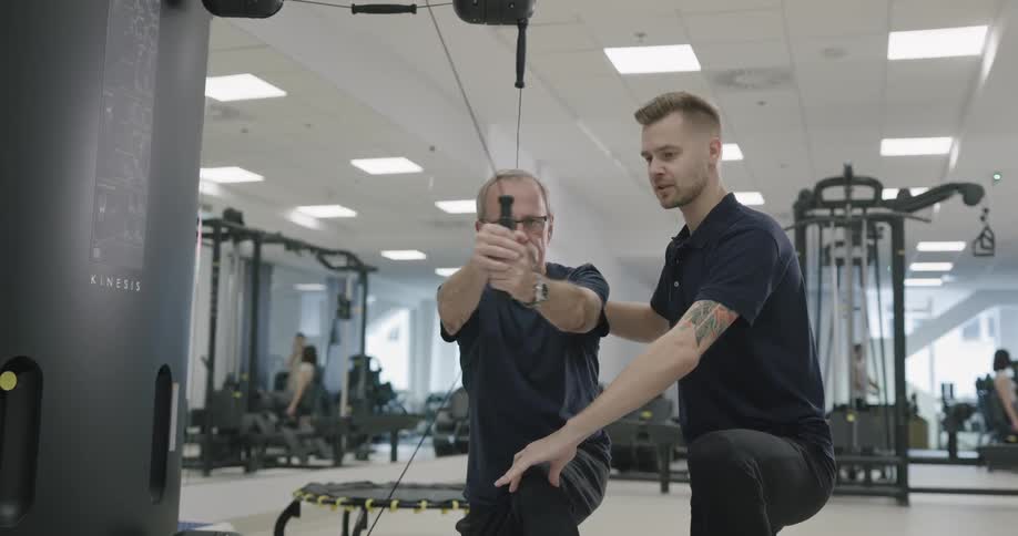 A young man shows an elderly man how to use exercise equipment at a gym