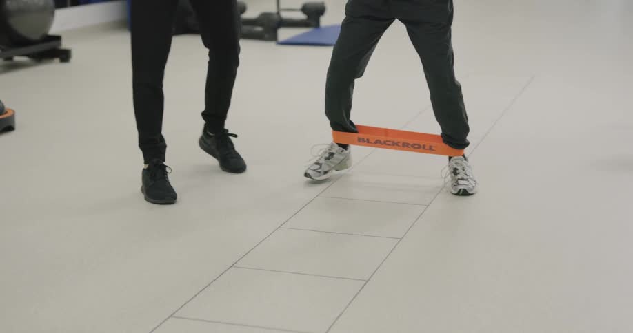A young man shows an elderly man how to exercise with a band on his feet