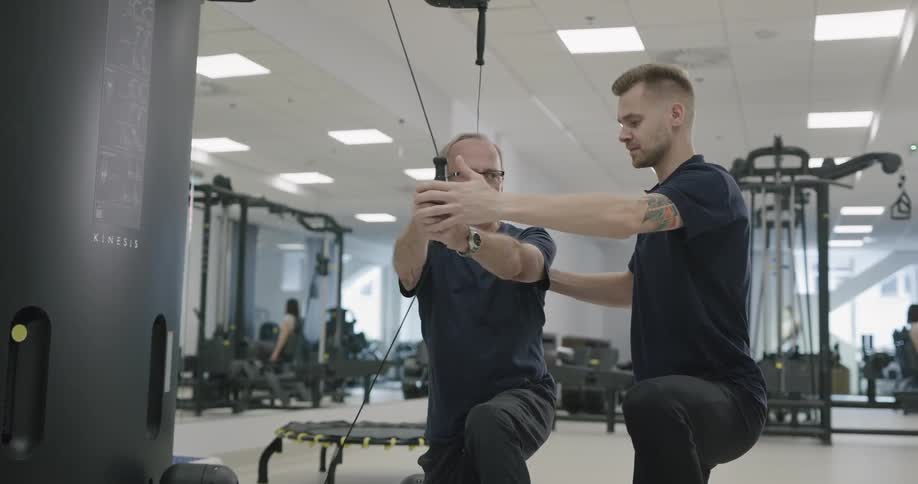 A physical therapist works with a man on fitness equipment in a clinic