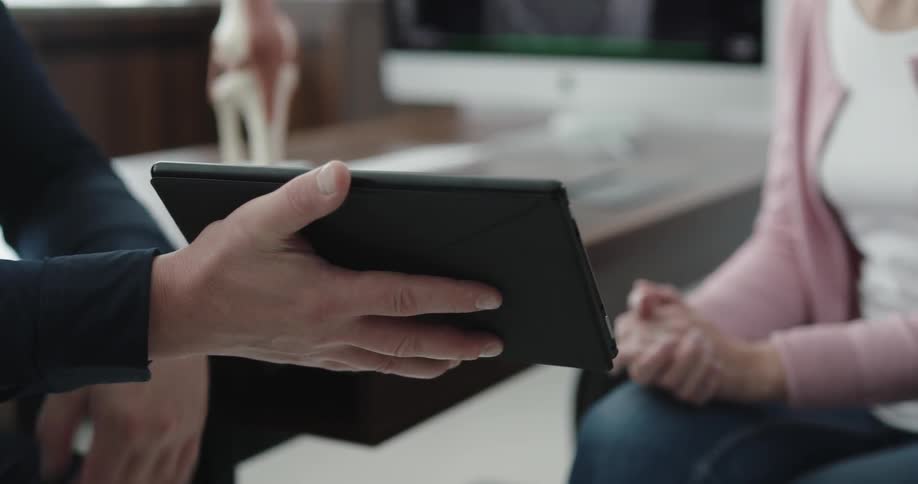 Doctor uses tablet and shows it to the patient in the office during daylight
