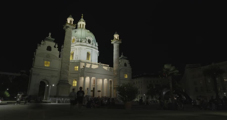 A baroque style church with domes and pedestrians at night