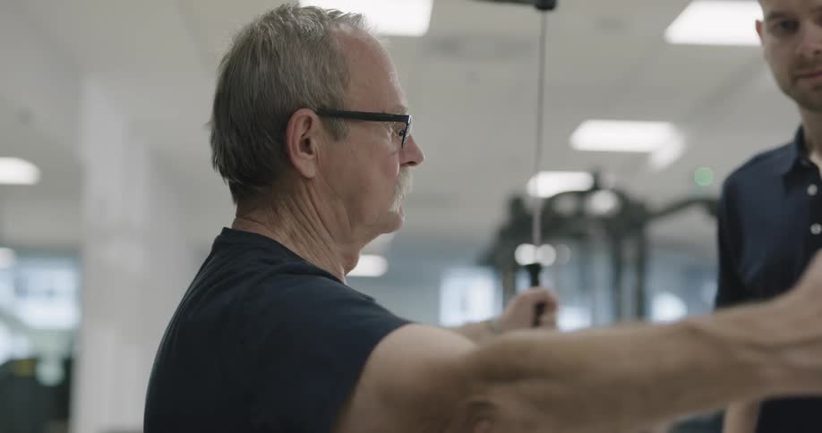 A man is working out in a gym with a trainer