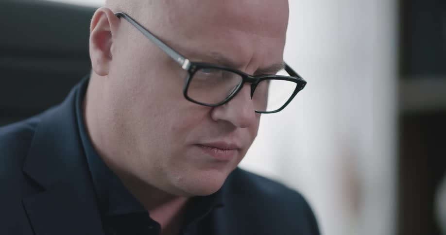 Male wearing black glasses and a suit reading on a tablet