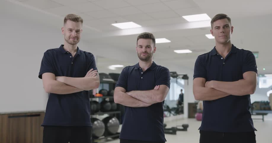 Three men are standing with their arms crossed in an exercise facility