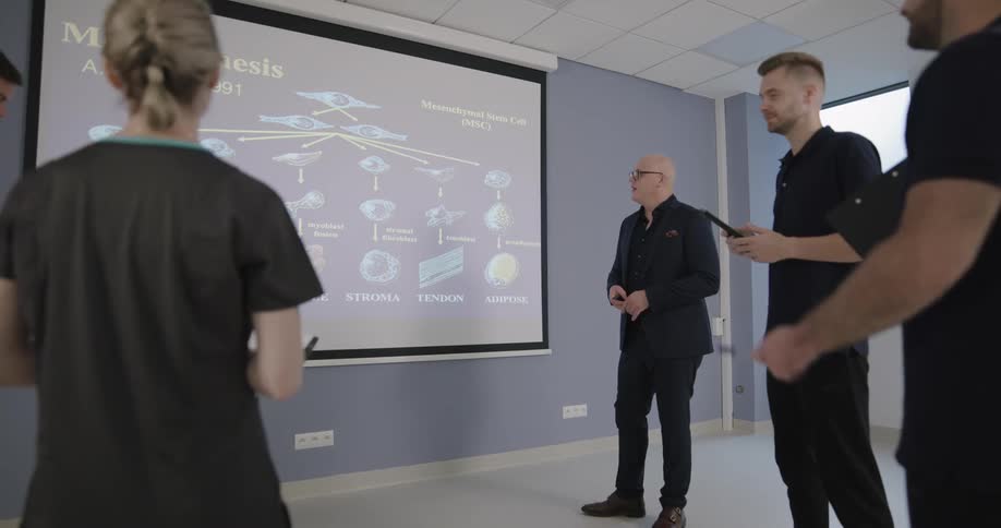 A team of medical professionals stands in front of a projector screen while discussing the projected slide about cellular differentiation