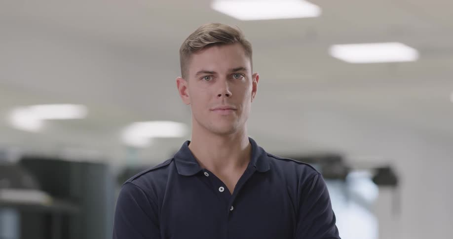 Man wearing dark blue polo shirt looks at the camera indoors during daylight
