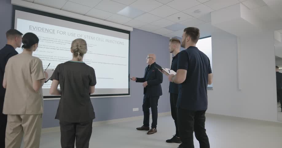 A group of people watch a man give a presentation on a large screen