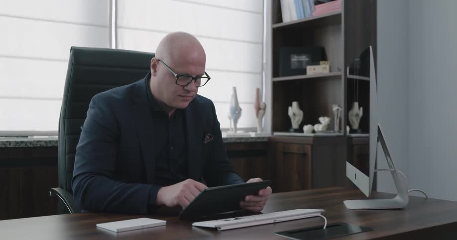 Man sits at desk in office studying tablet