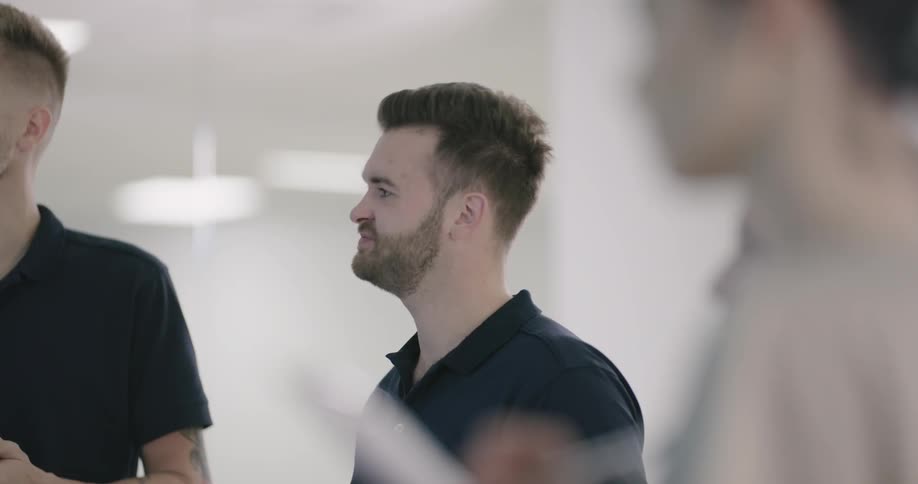 Man in a black polo shirt stands talking and nodding with others