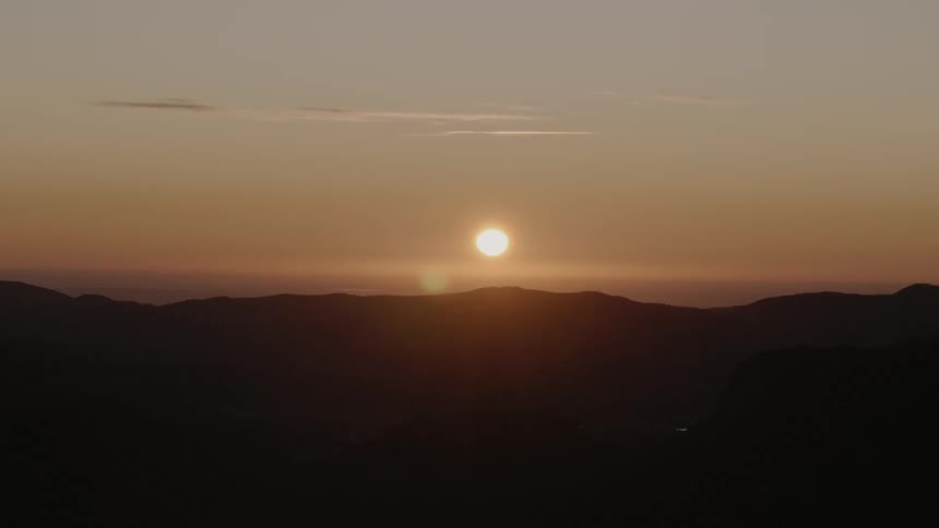 The sun sets in the sky behind the mountain