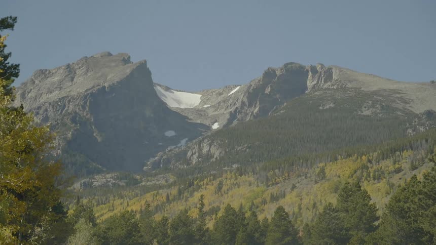 Snow topped peaks of a mountain range surrounded by pine trees and forests