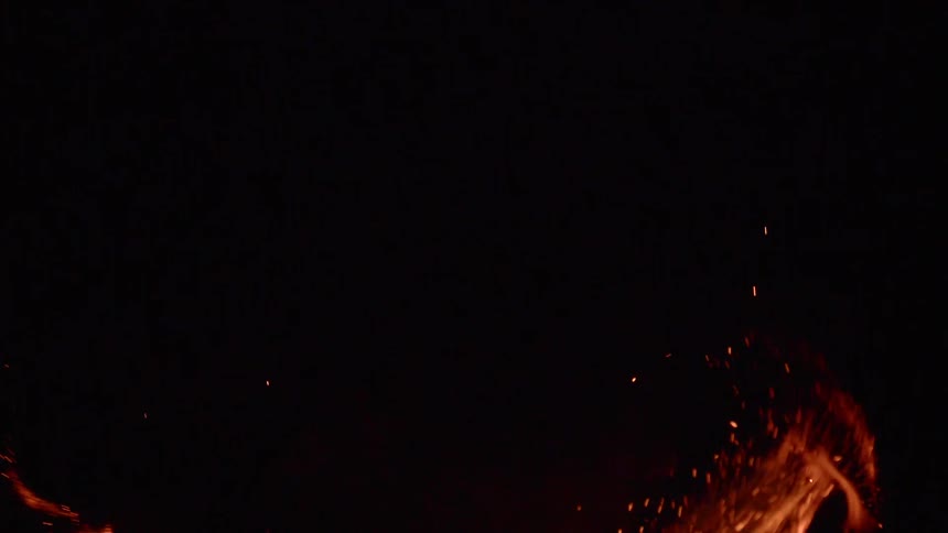 A fire burns and sends sparks into the air on an inky black background