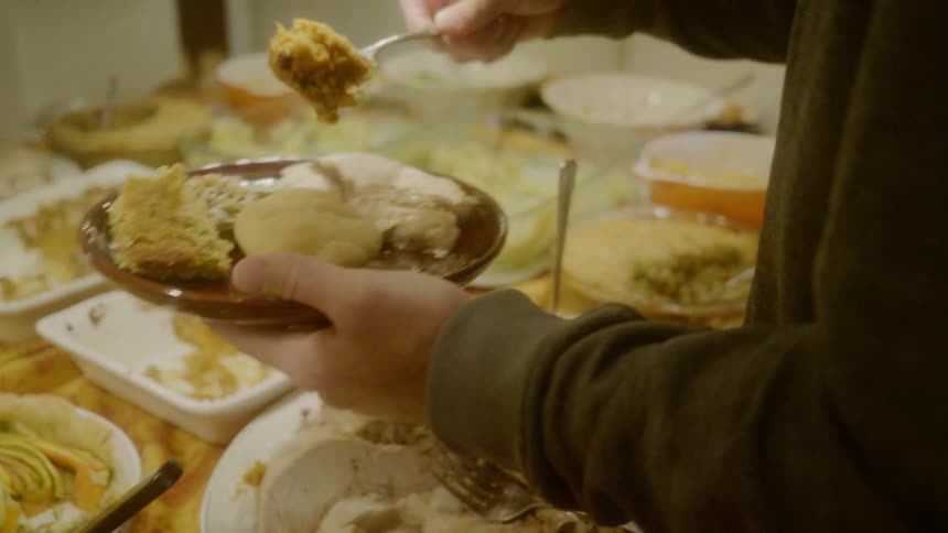 A man makes a plate of food from a large spread on a kitchen countertop
